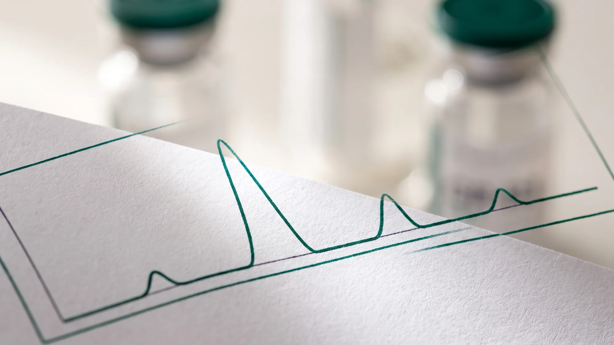 Close-up of the chromatogram peaks printed on a Certificate of Analysis, two vials behind it